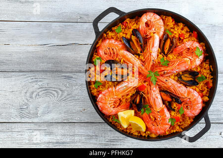 De délicieux fruits de mer paella de Valence avec les langoustines, les moules sur le riz et crémeuse salé avec des épices et des tranches de citron dans le moule, sur la vieille table en bois, au Banque D'Images