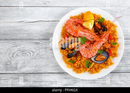 Partie de fruits de mer paella de Valence avec les langoustines, les moules sur le riz et crémeuse salé avec des épices et des tranches de citron sur la plaque, sur la vieille table en bois, Banque D'Images