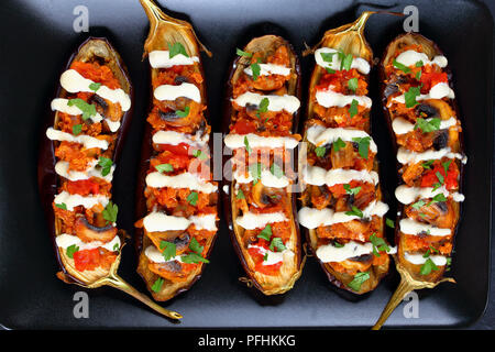 Close-up of delicious aubergines cuites au four farcies au quinoa, champignons, tomates et sauce Tahini sur la plaque noire, sain et facile méditerranée vegan rec Banque D'Images