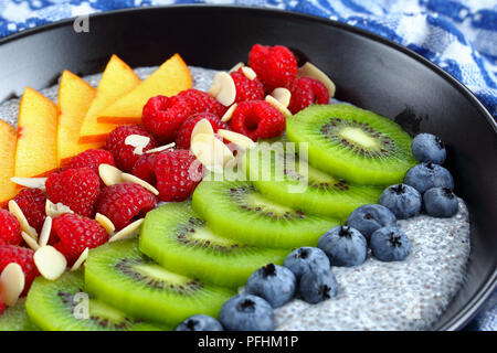 Petit-déjeuner sain- chia seeds délicieux pudding aux framboises, bleuets, pêches et kiwis en tranches bol noir sur la vieille table en bois, sélective Banque D'Images