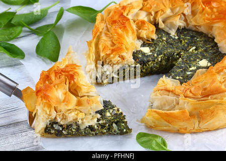 Golden delicious hot croûte à tarte feta épinards grecque ou spanakopita découper en tranches sur du papier blanc avec une spatule sur la pièce sur la table, recette, authentique Banque D'Images