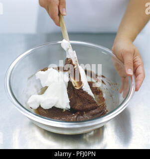 Les blancs d'œufs fouettés d'être plié dans une sauce au chocolat dans le bol en verre, high angle view Banque D'Images