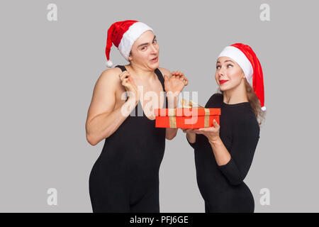 Coffret cadeau homme femme présents à santa hat. homme avec les bras levés à la caméra avec surpris à faire face. Nouveau concept de l'année. Studio shot, isolé sur gray b Banque D'Images