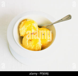 Trois boules de crème glacée mangue garni d'érable servi dans un bol blanc avec une cuillère, vue du dessus . Banque D'Images