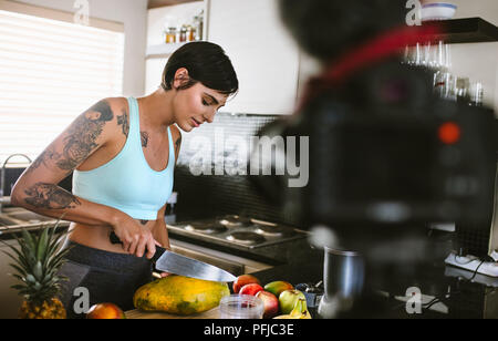 Jeune femme dans la cuisine l'enregistrement de vidéo sur l'appareil-photo. Les femmes travaillant sur la notion de fruits dans blogger cuisine. Banque D'Images