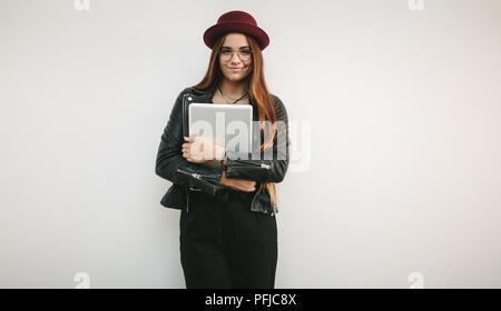 Portrait d'une femme portant des lunettes et un chapeau tenant un ordinateur portable. Smiling woman holding avec bras croisés. Banque D'Images