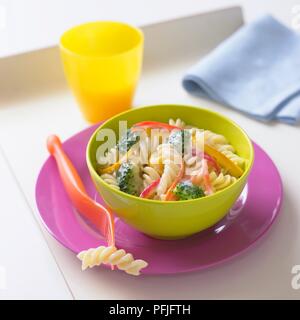 Bol de pâtes fusilli avec brocoli, carottes, poivrons dans la sauce au fromage, fourchette, serviette et tasse à proximité Banque D'Images