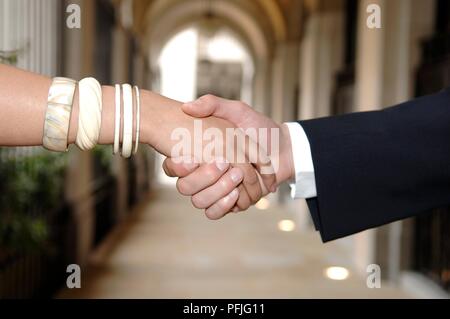 Jeune femme et jeune homme se serrer la main, femme portant des bracelets, homme portant costume, close-up Banque D'Images