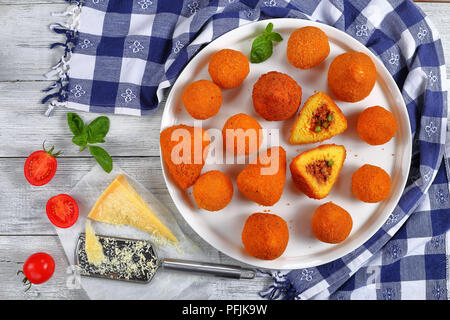 Arancini siciliens - risotto au safran et billes de cône farcies de viande et les pois verts ragoût sur le plateau de table en bois avec des serviettes de cuisine, l'huile d'olive sur b Banque D'Images