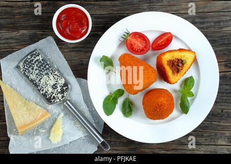 Arancini frits - une cuisine italienne classique, des cônes de risotto au ragoût, farcies de viande et les pois verts sur plaque blanche, sauce tomate, fromage parmesan sur t Banque D'Images