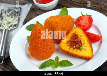 Arancini frits - une cuisine italienne classique, des cônes de risotto au ragoût, farcies de viande et les pois verts sur plaque blanche, la sauce tomate, le parmesan sur la table, Banque D'Images