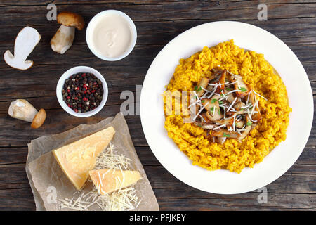 Safran délicieux risotto crémeux aux cèpes frits garnis de saupoudrée de persil et de parmesan râpé sur la plaque blanche sur table en bois foncé avec Banque D'Images