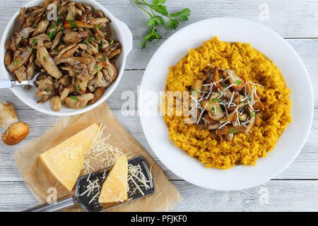 Safran délicieux risotto crémeux aux cèpes frits garnis de saupoudrée de persil et de parmesan râpé sur la plaque blanche sur table en bois avec ingrédients Banque D'Images