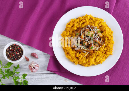 Safran délicieux risotto crémeux aux cèpes frits garnis de saupoudrée de persil et de parmesan râpé sur la plaque blanche sur le tapis de table, il authentique Banque D'Images