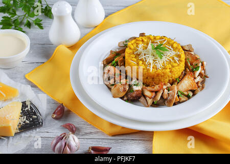 Safran délicieux risotto crémeux aux cèpes et persil frit avec du fromage parmesan râpé servi sur des assiettes blanches à la crème, une authentique cuisine italienne Banque D'Images