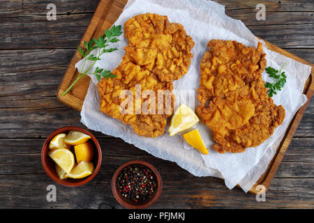 Golden delicious brown Wiener Schnitzel préparé sur recette authentique classique servi sur une planche à découper avec les quartiers de citron, sur une table en bois, vue d'un Banque D'Images