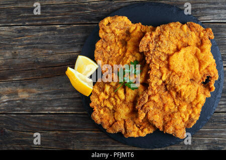 Golden delicious brown deux Wiener Schnitzel préparé à partir de tranches de veau aile de papillon, cut, servi sur la plaque en pierre noire avec des quartiers de citron et le persil, Banque D'Images