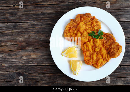 Golden delicious brown classic Wiener Schnitzel - escalopes de veau panées ou servi sur plaque blanche avec les tranches de citron sur la table en bois sombre, vue de abov Banque D'Images