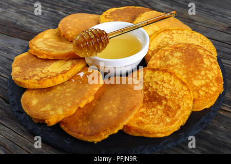 De délicieuses crêpes à la citrouille jaune doré noir sur plaque en pierre avec du miel dans le centre de table en bois sombre, vue de dessus, close-up Banque D'Images