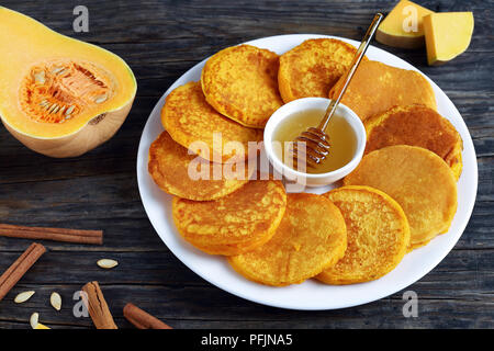 Crêpes de potiron délicieux avec du miel dans le centre de la plaque blanche , sur table en bois foncé avec des bâtons de cannelle, morceaux de citrouille sur arrière-plan, Vue de côté Banque D'Images