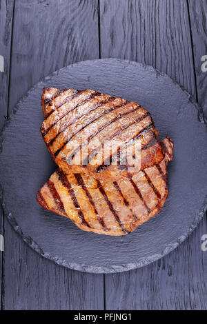 Deux steaks de boeuf grillé marbré de noir avec des rayures sur le plateau en ardoise sur table en bois noir, vertical Vue de dessus Banque D'Images