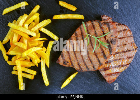 Fun pour de délicieux steaks de bœuf grillé avec des rayures sur la plaque en ardoise noire servis avec frites, vue d'en haut Banque D'Images