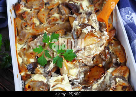 Close-up of delicious en cocotte aux champignons des bois et sauce à la crème aigre dans plat à gratin sur de vieilles planches en bois avec une cuillère de bois, vue du dessus Banque D'Images