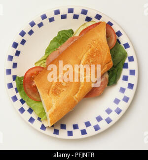 Sandwich Baguette farcie au jambon, tomates et feuilles de laitue, sur une plaque blanche avec motif bleu sur les bords, vue de dessus Banque D'Images