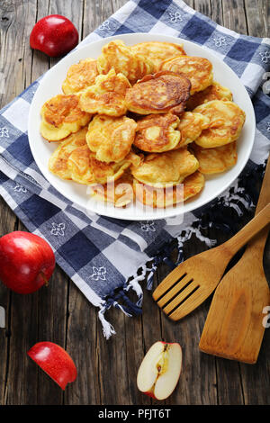 De délicieuses crêpes chargé avec des morceaux de pommes juteuses, sur plaque blanche sur la vieille table en bois foncé avec des spatules et les pommes à l'arrière-plan, vue verticale fr Banque D'Images