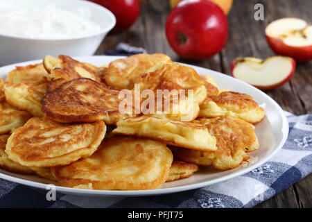 Pancakes moelleux savoureux chargé avec des morceaux de pommes juteuses, sur plaque blanche sur la vieille table en bois foncé avec de la crème dans un bol et les pommes au fond, sid Banque D'Images