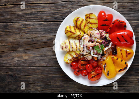 De délicieux fruits de mer épicés salade avec vinaigrette citron servi sur plaque blanche avec légumes grillés, vue de dessus Banque D'Images