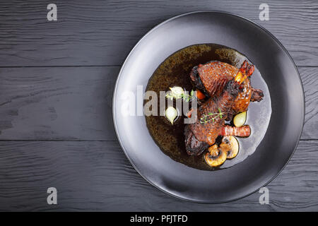 Portion de ragoût de poulet savoureux - braisé de cuisse et le pilon avec le vin, les herbes, les champignons et les légumes servis sur la plaque noire sur la table en bois, ambiance festive Banque D'Images