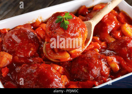 Close-up de cuillère en bois avec un braisé en sauce tomate aux boulettes et des légumes au fond d'un plat allant au four avec des boulettes de viande, côté Vue du dessus Banque D'Images