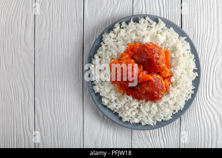 Chaud savoureux braisé Boulettes de dinde à la sauce tomate et légumes servi avec du riz long grain sur une plaque gris sur table en bois blanc, vue d'en haut Banque D'Images