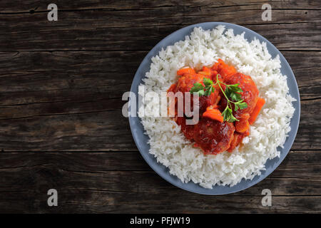 Chaud savoureux braisé Boulettes de dinde à la sauce tomate et légumes servi avec du riz long grain sur une plaque gris sur table en bois sombre, vue d'en haut Banque D'Images
