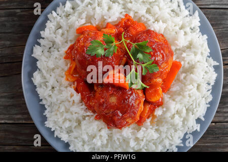 Close-up of snacks braisé Boulettes de dinde à la sauce tomate et légumes servi avec du riz long grain sur une plaque gris sur table en bois foncé, sain Banque D'Images