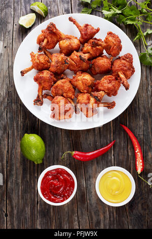 Frits savoureux poulet croustillant battues avec des ailettes de bout d'os sur une plaque blanche sur table en bois foncé avec de la moutarde et du ketchup en sauce à bateaux Banque D'Images