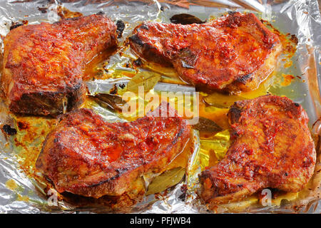 Tendres rôtis au four, épicé et juteux côtelettes de porc sur du papier d'aluminium sur le plat, vue de dessus, close-up Banque D'Images