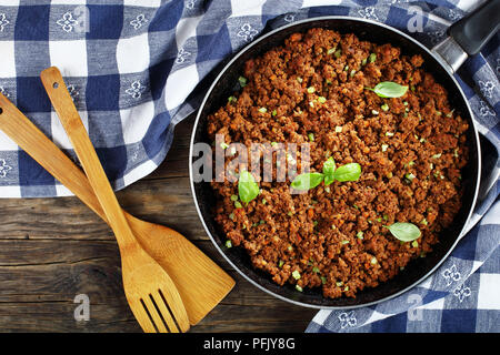 - Hot sauce bolognaise boeuf juteux à l'étuvée avec la sauce tomate, les épices, le basilic, haché finement les légumes et le céleri dans la poêle sur la table en bois avec Banque D'Images