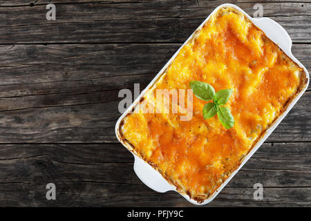 De délicieux plats italiens en couches avec feuilles de pâte à lasagne bolognaise, ragoût et garnie de fromage fondu et de feuilles de basilic frais dans le plat de cuisson sur le vieux dark Banque D'Images