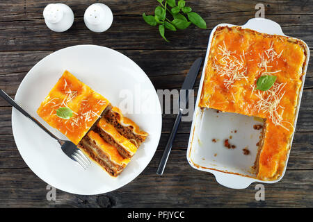 Partie de délicieux lasagne italienne garnie de fromage fondu et de feuilles de basilic frais, saupoudré de parmesan râpé sur la plaque blanche et dans un Banque D'Images