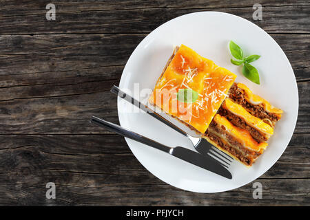 Partie de délicieux lasagne italienne garnie de fromage fondu et de feuilles de basilic frais, saupoudré de parmesan râpé sur la plaque blanche avec une fourchette Banque D'Images