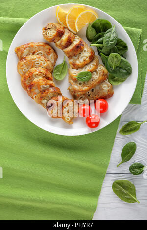 Tranches de salé désossé farci poulet pilons avec des pâtes, de la viande hachée et légumes servi avec bébés épinards, tomates et les tranches de citron sur whit Banque D'Images