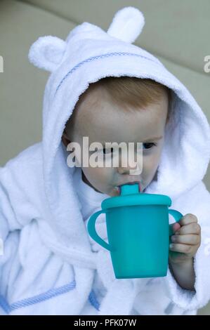 Baby Boy wearing peignoir avec un capuchon sur l'alcool, à partir de la tasse en plastique avec bec, close-up Banque D'Images