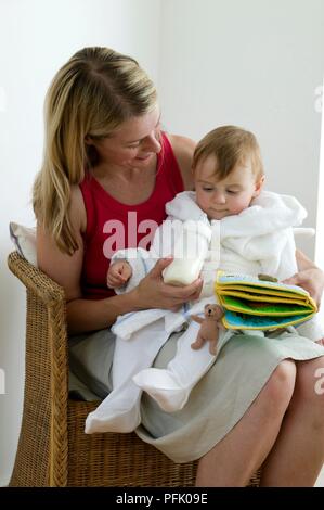 Femme assise avec petit garçon sur ses genoux, tenant une bouteille de lait, close-up Banque D'Images