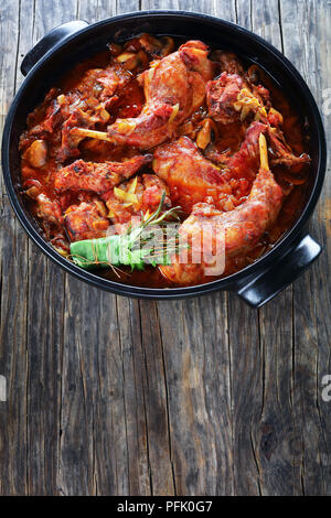 Lapin braisé à l'italienne avec le poireau haché, tomates, herbes et champignons dans la cocotte sur la vieille table en bois foncé, vertical Vue de dessus Banque D'Images