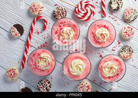 Pas de cuire Noël ou Nouvel An dessert - Mousse au fromage garni de crème fouettée et de miettes de rose bonbon en verre tasses sur la table avec des cannes de bonbon et Banque D'Images