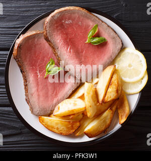 Pavé de boeuf est servi avec pommes de terre rôties et de citron sur une plaque sur un tableau noir. haut Vue de dessus Banque D'Images