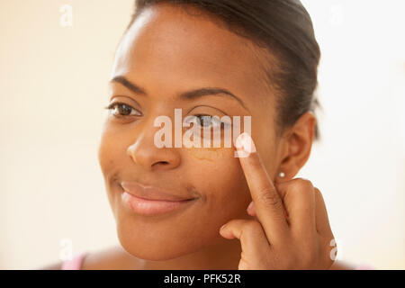 Femme d'appliquer de l'huile à l'aide de la zone sous les yeux du bout de doigt Banque D'Images