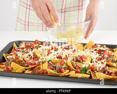 Jeune femme. Saupoudrer de fromage râpé les croustilles au maïs, tomates, oignons hachés et de coriandre sur une plaque de cuisson Banque D'Images